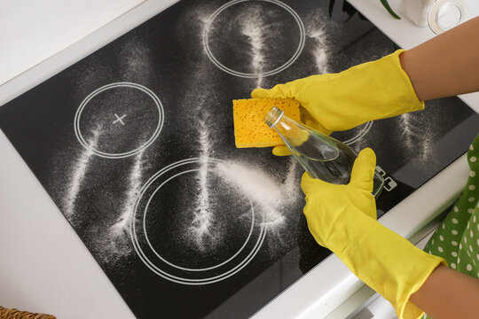 Housewife cleaning electric stove with vinegar and baking soda in kitchen, closeup