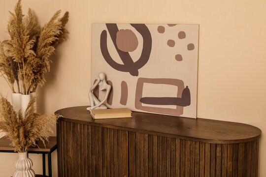 Chest of drawers, pampas grass in vases and picture near brown wall in room. Closeup