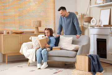 Fototapeta premium Happy father and his daughter in sweaters with teddy bear reading book at home