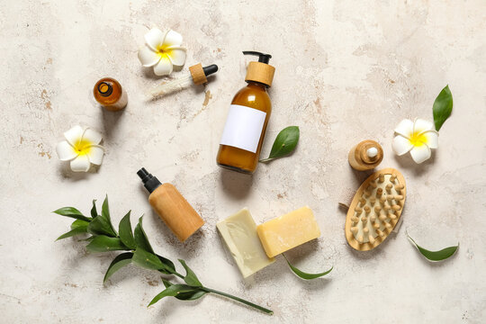 Composition with bottles of shampoo, soap bars and plumeria flowers on beige grunge background