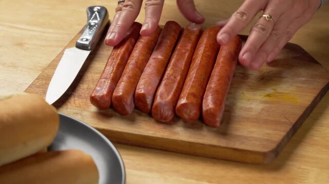 Hands preparing vacuum packed sausages for cooking on a wooden cutting board