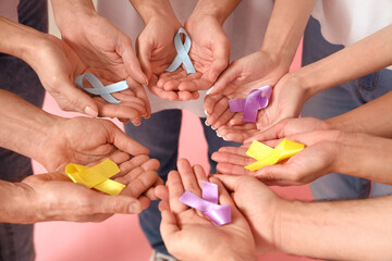 Fototapeta premium People with different awareness ribbons on pink background, closeup. World Cancer Day