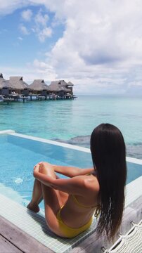 Luxury resort travel vacation destination overwater bungalow villa woman relaxing by pool. Social media influencer traveler luxurious high end lifestyle. Raw unedited vertical video of real woman.
