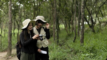 Fototapeta premium Two Asian Women Photographers Checking Pictures On Camera In Forest