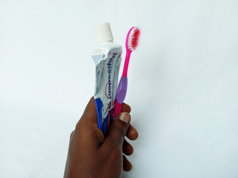 African holding empty Pepsodent toothpaste tube, used, red, pink toothbrush on white background. Not good for oral hygiene, unable to remove food particles. Kumasi, Ghana - December 9, 2025