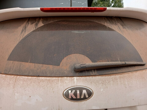 Dirty rear windscreen of white Kia car after riding, driving on dusty road. Back view of Honda CR-V window. Black wiper at back side wiping, semicircle shape on glass. Kumasi, Ghana - January 30, 2026