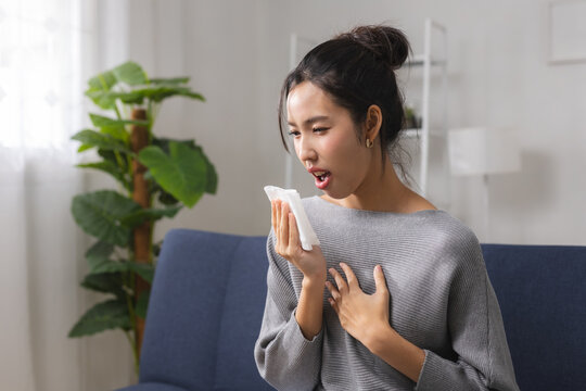 Allergy and cold symptoms concept, woman holding tissue before sneezing while sitting at home, experiencing nasal irritation, seasonal allergies and respiratory discomfort.