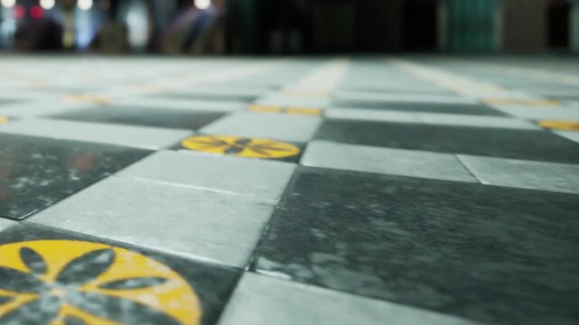 A checkerboard pattern of black and white tiles covers the floor. Yellow flower patterns are visible among the tiles in an indoor area, likely a public place.