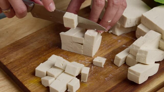 Cutting fresh tofu into cubes on a wooden cutting board