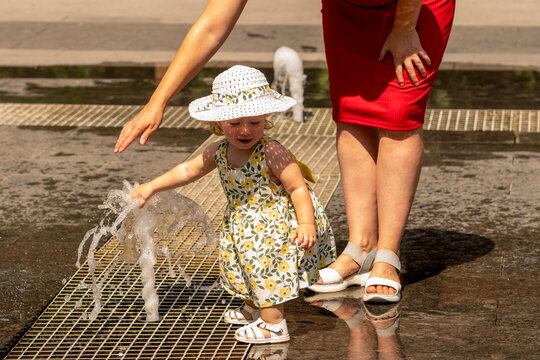 Toddler Girl Touching Splash Fountain With Mother Nearby