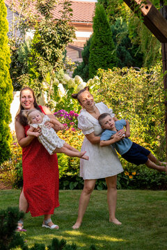 Women Swinging Children Sideways During Playful Garden Game