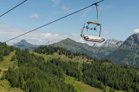 Col dei Baldi, Italy. Empty chairlift above alpine forests and meadows with Dolomite mountain panorama