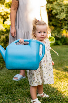 Young Girl Carrying Oversized Blue Watering Can Outdoors
