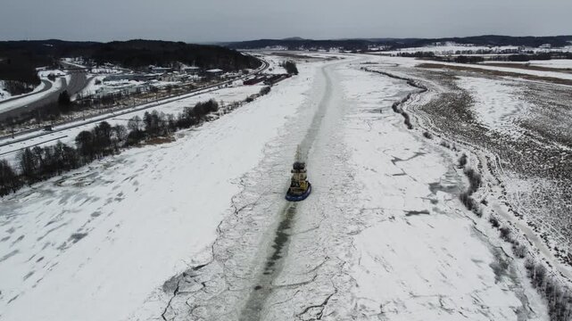 Icebreaker ship moving through frozen Gota alv river at Alvangen, Sweden in winter, aerial upward tilt follow