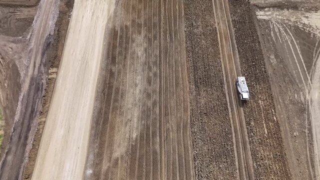 Construction machine performs earthworks across agricultural terrain at Barabasca logistics park near Fiorenzuola d'Arda, Piacenza, Emilia-Romagna, Italy, preparing ground, drone slide.
