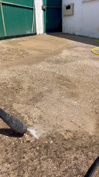 Horizontal shot of a pressure washer cleaning a stained concrete floor, clearly revealing the contrast between the dirty surface and the freshly cleaned area.