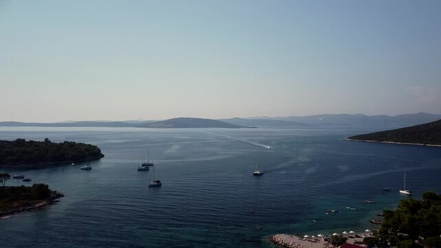 Maslinica, Croatia islands and anchored boats spread across calm Adriatic Sea, aerial pan right establishing overview of harbor