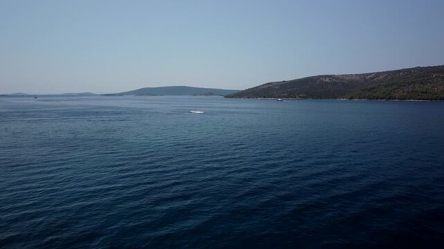 Adriatic Sea and low islands extend beyond Seget Vranjica, Trogir, Croatia, aerial slow dolly forward, peaceful serene backdrop as boat turns
