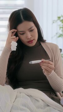 Asian woman holding a medical thermometer for measuring body temperature