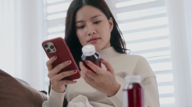 Female Asian holding medicine bottle reading smartphone for health information