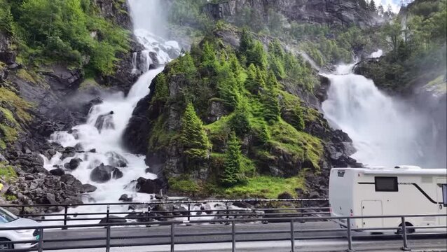 Motorhome Driving Across Stone Bridge in Front of Powerful Latefossen Twin Waterfall in Odda Norway