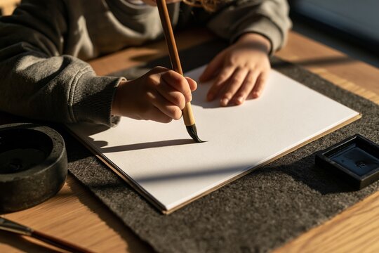 Child hands holding a calligraphy brush over blank paper