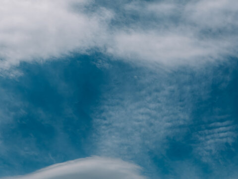 Textured cloud layers over deep blue sky, atmospheric nature background.