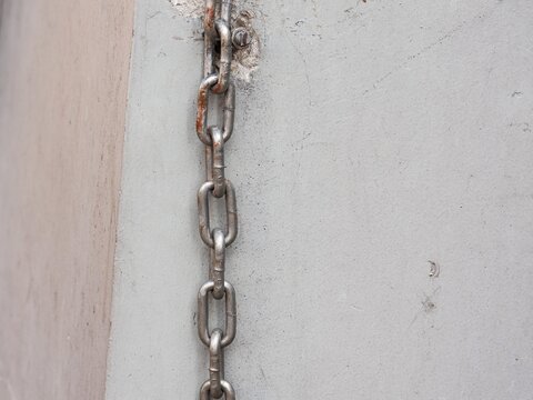 Vertical steel metal link chain anchored to a concrete wall surface with slight rust spots.