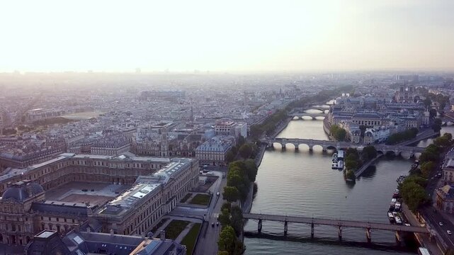 Aerial drone footage over seine river showing historical cityscape bridges and ile de la cite in paris at sunrise.