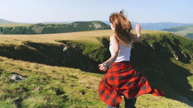 Person dances on grassy hill with a view of mountains on a sunny day in the countryside