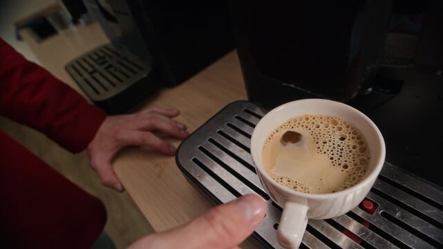 Young adult Caucasian man with glasses taking cup of freshly brewed coffee from machine, drinking with satisfaction, and walking away. Ideal for corporate breakroom marketing campaigns