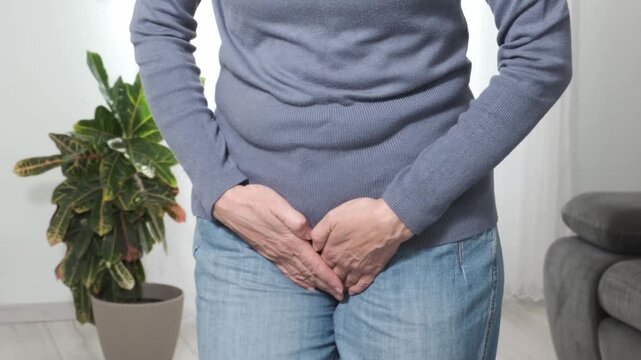 Back pain. Middle aged woman holding her lower back and massaging it with her hands at home. Close-up, rear view, side view. Lumbago, sciatica, lower back pain, lumbago in the back, hernia, protrusion