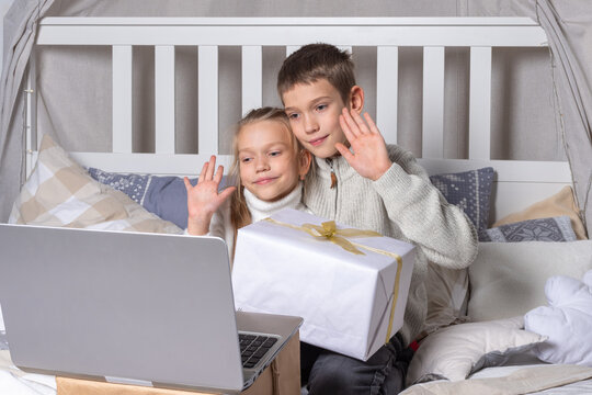 Preschool children holding gift box chatting via video link via laptop and waving hand greeting relatives or friends at home