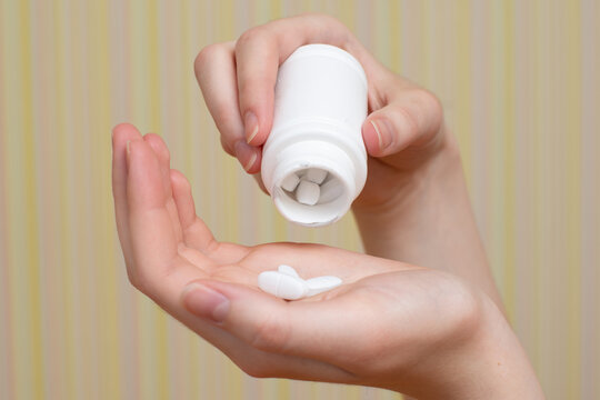 Close-up of a female hand pouring out white tablets, vitamins for the treatment of a pandemic . Health concept