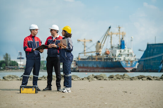 Three marine engineers discussing ship inspection and maintenance plans near cargo vessel, working together at industrial shipyard with copy space.