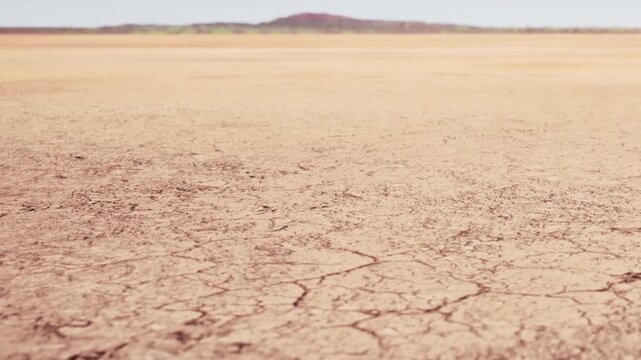 Dry cracked earth stretching far into the distance with a small hill visible in the background. The open area is without any water or vegetation and has a bright sky above.