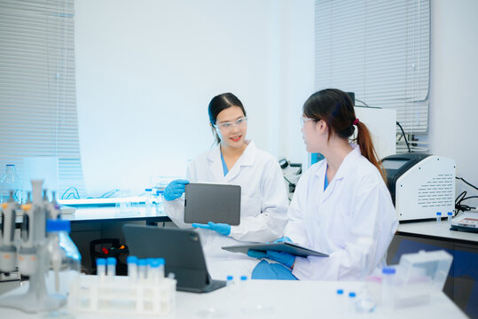 Asian female scientists conducting research with a micropipette and digital tablet in laboratory.