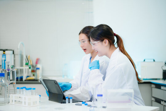 Asian female scientists conducting research with a micropipette and digital tablet in laboratory.