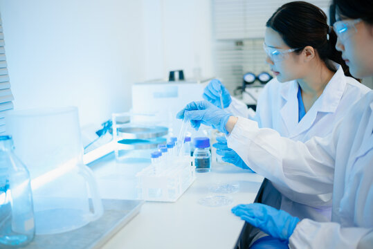 Asian female scientist holding a test tube with liquid sample during scientific research in a modern biotechnology laboratory.