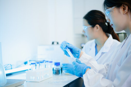 Asian female scientist holding a test tube with liquid sample during scientific research in a modern biotechnology laboratory.