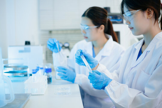 Asian female scientist holding a test tube with liquid sample during scientific research in a modern biotechnology laboratory.