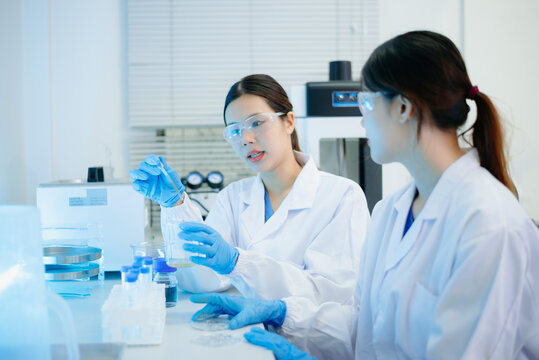Asian female scientist holding a test tube with liquid sample during scientific research in a modern biotechnology laboratory.