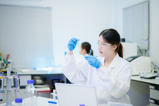 Female scientist analyzing data on laptop with chemical test tube samples in a modern biotechnology laboratory.