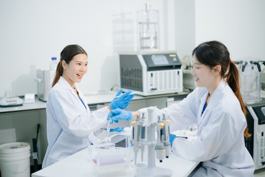 Asian female scientists conducting research with a micropipette and digital tablet in laboratory.
