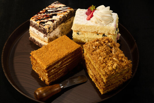 Four pieces of different cakes on a tray on a black background