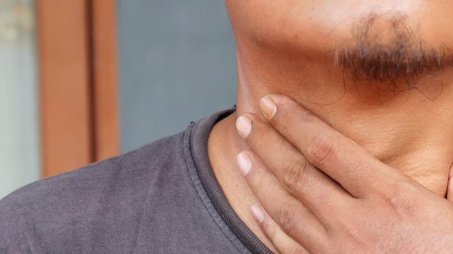 Asian man hand on sore throat attack. A view of male hand on sore throat because of pain attack indoor.