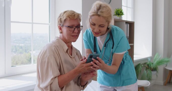 Nurse or doctor guides senior patient during checkup in clinic explains a medical app on smartphone, showing records, scheduling options, and telehealth features. Digital healthcare and support.