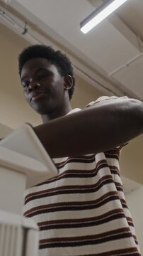 Vertical shot of young adult African American man operating office printer, scanning documents and pressing buttons. Footage represents corporate administration and workplace technology use