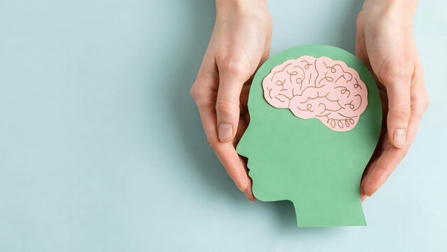 Hands holding a green cutout of a human head silhouette with a brain icon