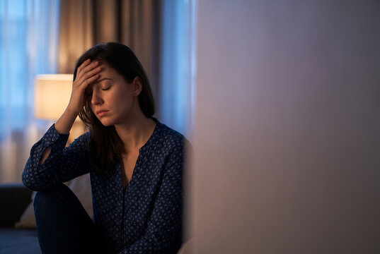 Young woman sitting indoors with thoughtful expression touching her head